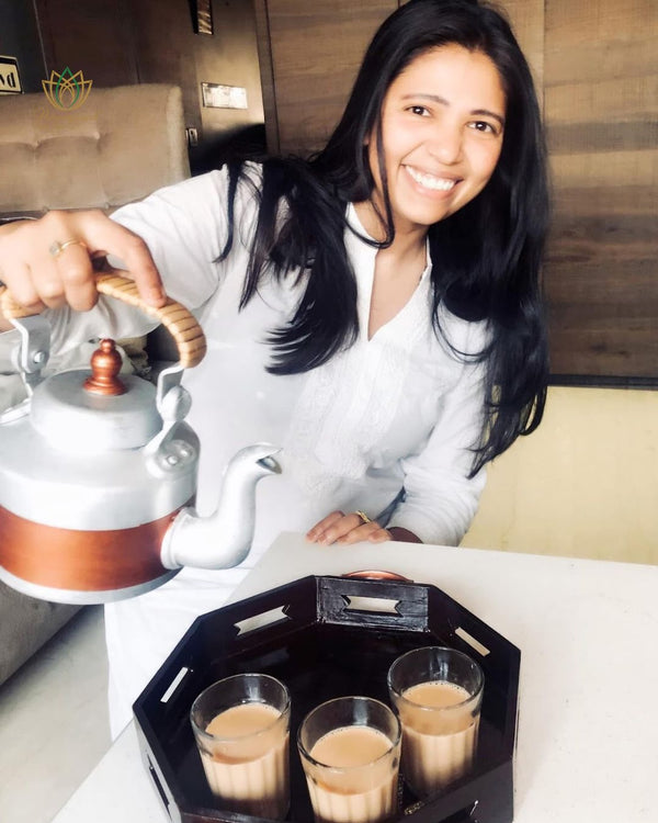 Woman serving tea from a copper kettle with glasses on a black tray