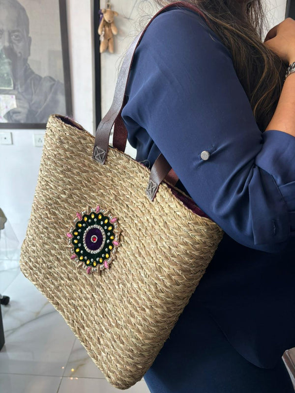 Natural sabai grass basket bag with a beaded medallion carried on the shoulder