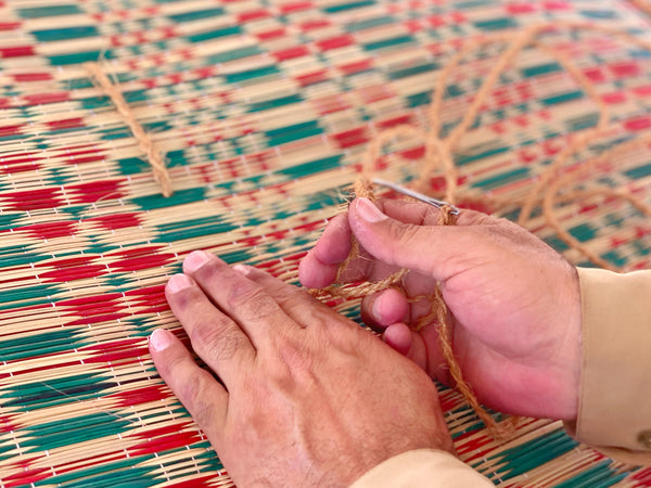 Artisan's hands weaving a red and green grass mat