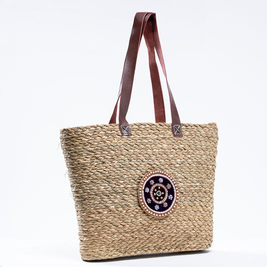 Front view of Indrani Sabai basket bag with handwoven body, leather handles, and beaded medallion