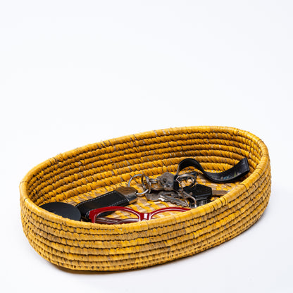 Yellow oval basket used as a catchall tray containing keys, glasses, and small personal items.